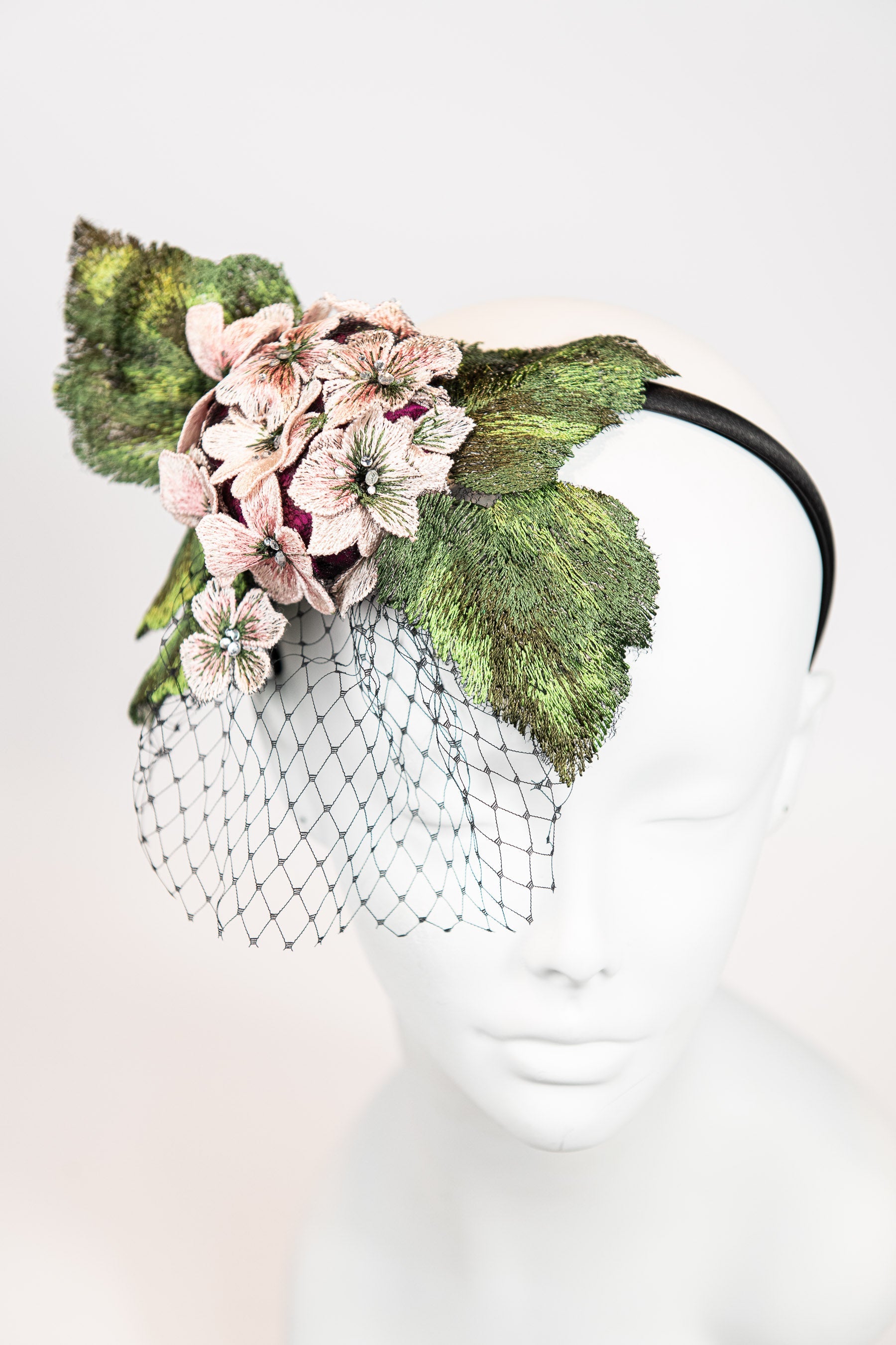 Fascinator headpiece with pink hydrangeas, large green leaves, and black birdcage netting