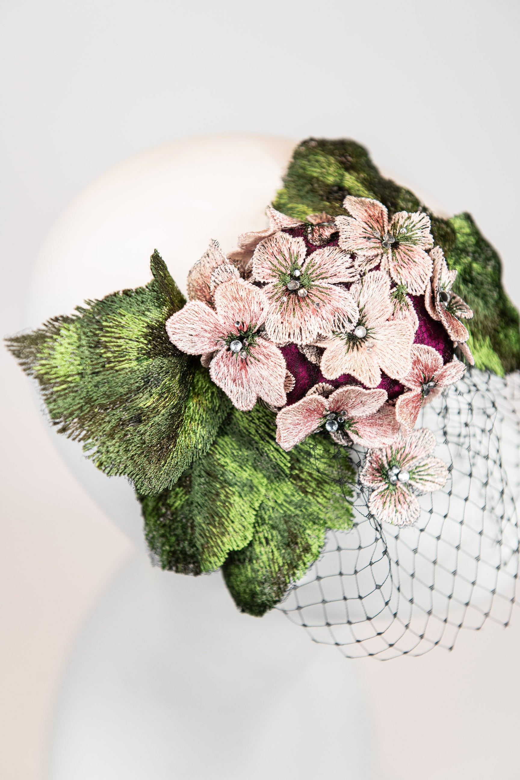 Fascinator headpiece with pink hydrangeas, large green leaves, and black birdcage netting