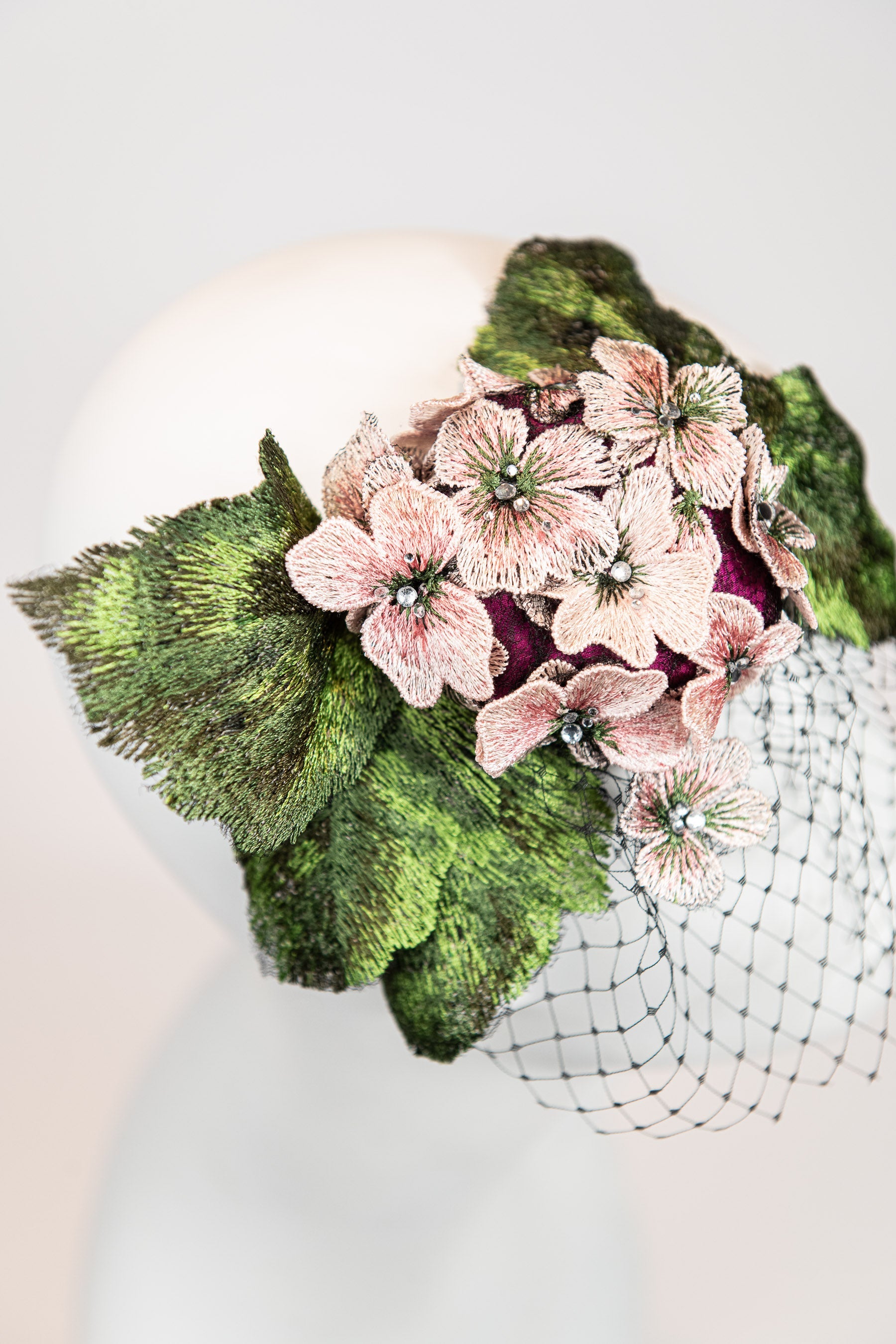 Fascinator headpiece with pink hydrangeas, large green leaves, and black birdcage netting