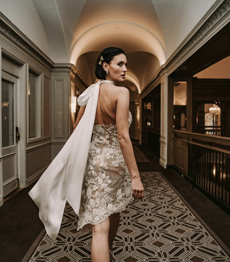 Woman in a floral dress with a white shawl walking down a hallway.